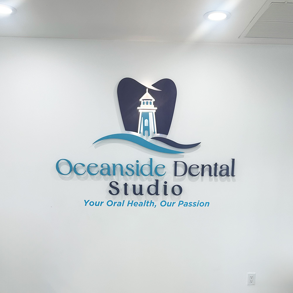 The image shows an interior wall with a sign that reads OCEANSIDE DENTAL STUDIO prominently, accompanied by a logo featuring a stylized lighthouse and waves, against a backdrop of a clean, modern office environment.