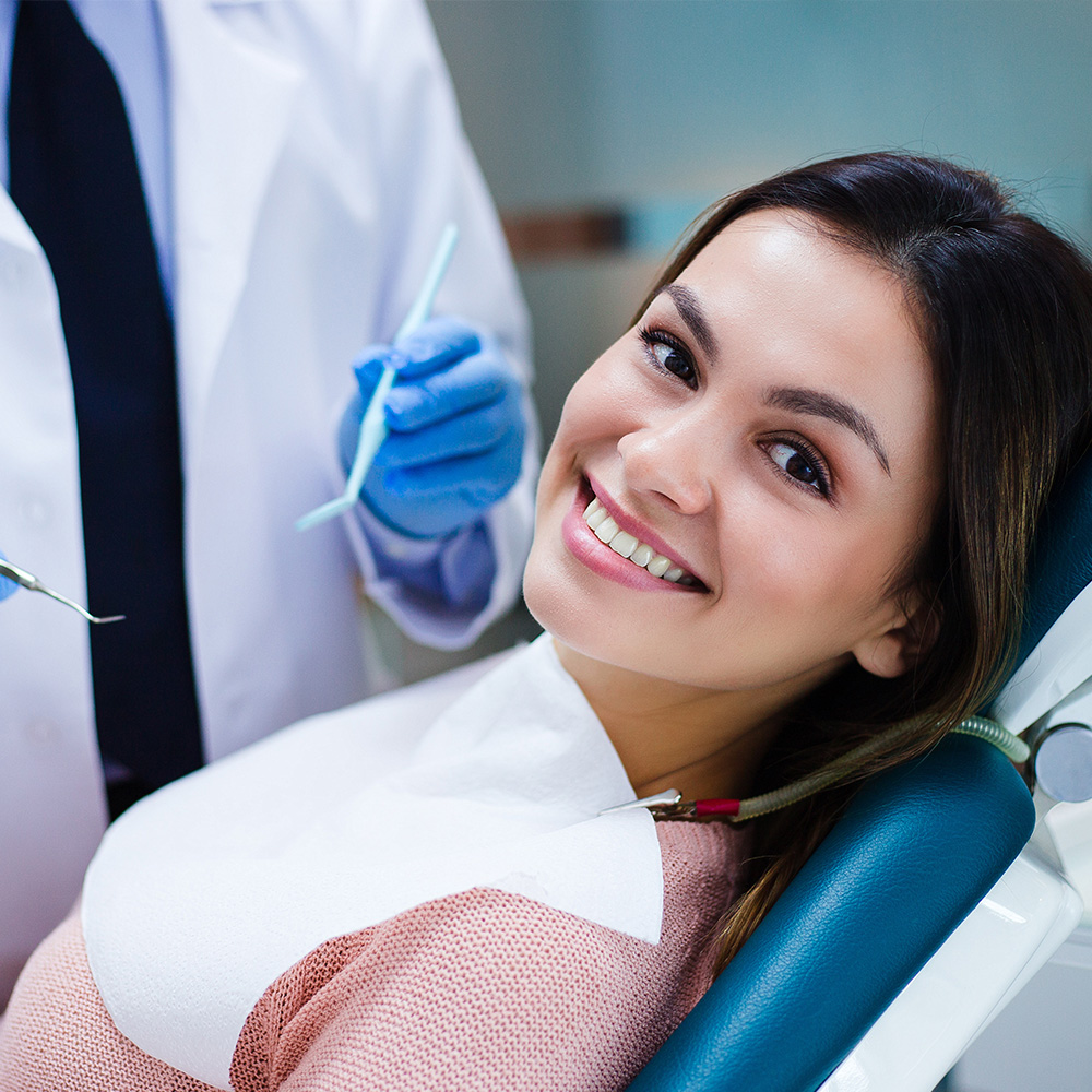 A dental hygienist is preparing a patient for a dental procedure while the patient smiles and appears relaxed.